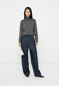 Pulôver cinza de gola alta com um acabamento texturizado, combinado com calças de ganga escuras de perna larga. Acessório com uma pequena bolsa branca.