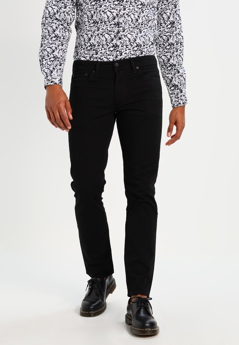 Černé skinny džíny vyrobené z denimu, s klasickým designem pěti kapes, poutky na opasek a hladkou texturou, spárované s košili s vzorem a botami.