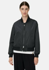 Schwarze Bomberjacke aus glattem, leichtem Stoff. Mit Reißverschluss vorne, gerippten Ärmelbündchen und Seitentaschen. Einfaches, klassisches Design.