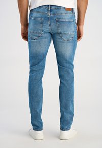 Blaue Denim-Jeans, Slim Fit, mit mittelhoher Taille, fünf Taschen und dezentem Verblassen. Abgeschlossen mit einem Lederetikett am hinteren Bund.