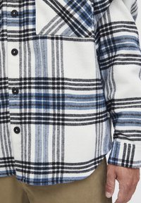 Hemd aus Flanell in Weiß mit schwarzem und blauem Karo-Muster, ausgestattet mit schwarzen Knöpfen und einem leicht geschwungenen Saum, gefertigt aus weichem Stoff.