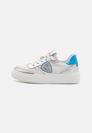 Sneaker têxtil branco com detalhes em prata, um puxador azul no calcanhar e um elemento decorativo texturizado em azul. Biqueira redonda com sola branca.