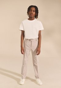 T-shirt bianca a girocollo, pantaloni grigio chiaro con trama, passanti per cintura e chiusura con bottone, abbinati a sneakers bianche.