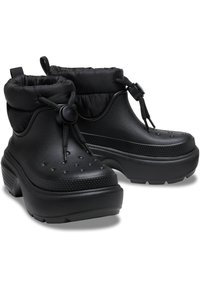 Botas impermeables negras con un acabado texturizado, puño elástico y cordón ajustable. Presentan perforaciones y acentos elevados para mejorar el agarre.