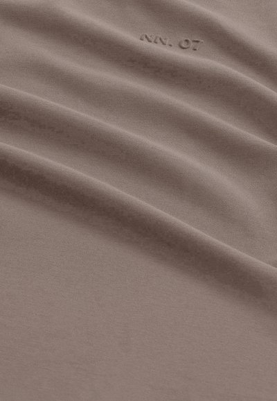 Tissu taupe avec de subtils plis diagonaux et texte embossé "K.N. 07" près du centre supérieur.