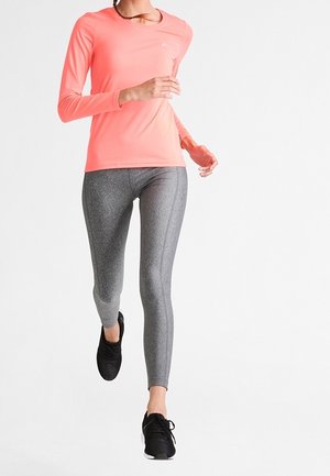 Długo-sleeve, jasnoróżowa koszula z okrągłym dekoltem, zestawiona z fakturowanymi szarymi legginsami i czarnymi butami sportowymi, model w pozie biegowej.