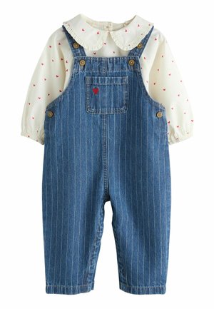 Denim-Overall mit vertikalen Streifen, dunkelblauer Farbe, versehen mit einer Vorderentasche mit einem roten Herzen, kombiniert mit einer weißen Bluse mit roten Herzmustern.