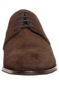 Chaussures à lacets en suède marron avec une texture lisse, dotées de lacets bleu foncé et d'une forme arrondie à l'avant. Semelle robuste avec peu de détails.