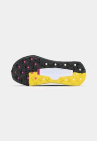 Black and yellow athletic shoe sole with a textured grip pattern, featuring pink accents, and a prominent white logo in the center.