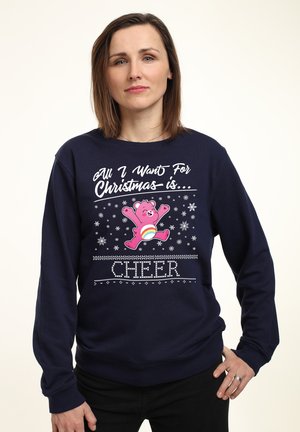 Marineblå sweatshirt med et pink bjørne grafik med teksten "Alt, jeg ønsker mig til jul er... GLÆDE," snefnug og dekorerede mønstre.