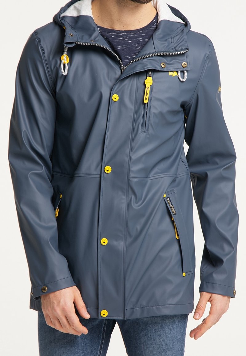Veste bleu marine imperméable avec une finition texturée, matériel jaune, poches zippées et une capuche doublée de doux matériau blanc.