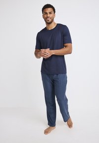 Marineblauwe t-shirt met korte mouwen gecombineerd met gestreepte pyjama broek. Zachte stof, relaxte pasvorm en een simpel ontwerp. Staande op blote voeten, met de armen ontspannen.