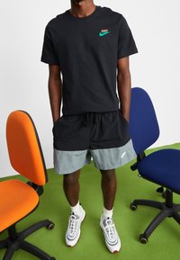 Černé tričko Nike s tyrkysovým logem, doplněné černými a šedými kraťasy s šňůrkou a emblémem Nike. Šedé tenisky s bílými akcenty.