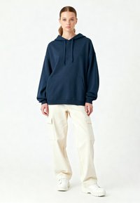 Hanorac supradimensionat bleu marin, cu buzunar frontal și șnur, asortat cu pantaloni cargo crem care au buzunare laterale și adidași albi.