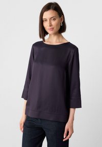 Top in satin viola scuro con scollo a barca, maniche a tre quarti e orlo dritto. Abbinato a pantaloni in denim scuro, con una texture liscia.