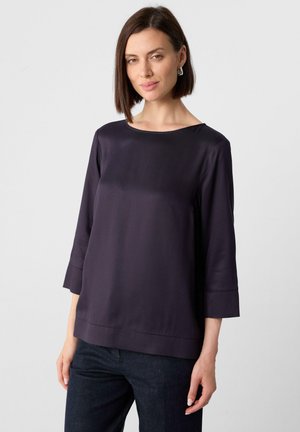 Dark purple satin top with a boat neckline, three-quarter sleeves, and a straight hem. Paired with dark denim trousers, smooth texture.