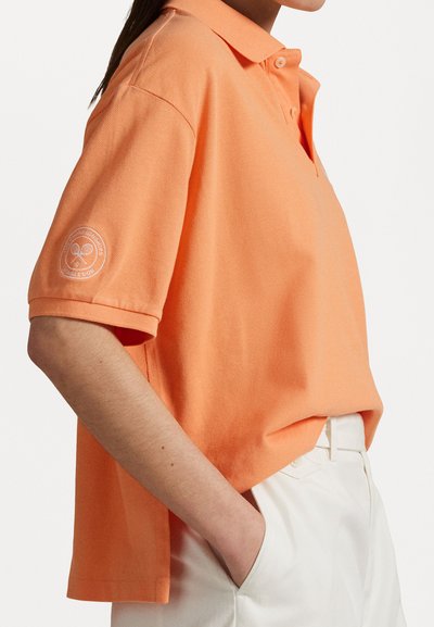 Polo tričko s krátkym rukávom v pastelovo oranžovej farbe, textúrovaná látka, trojgombíková légou a bielym logom na ľavom rukáve.