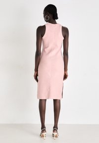 Form-fitting, sleeveless dress in soft pink fabric, knee-length with side slits, featuring a round neckline and minimal stitching detail.