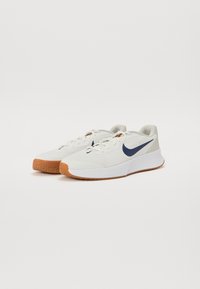 Bijele sportske tenisice s teksturiranim materijalom, mornarsko plavi Nike swoosh i gumeni potplat. Imaju debelu petu i dizajn na vezanje.