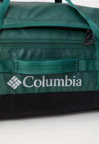 Green nylon duffel bag with black base, featuring a top zipper, webbed carrying handles, and Columbia logo in white.