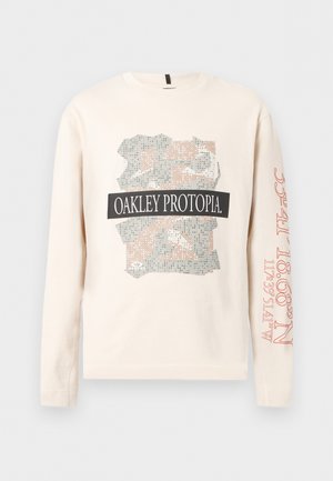 Cămașă bej cu mâneci lungi, cu imprimeu camuflaj abstract și textul "OAKLEY PROTOPIA" pe partea din față, coordonate roșii imprimate pe mânecă dreaptă.