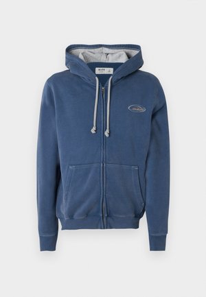 Blå hettejakke med glidelås laget av mykt materiale. Har en gråfôret hette, frontlommer og et lite logopatch på brystet.