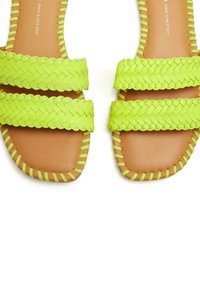 Sandali piatti intrecciati verdi con due cinturini. La suola è color sabbia e i bordi presentano una cucitura verde brillante. Design minimalista, stile con punta aperta.