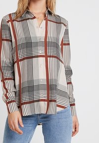 Button-up shirt with a beige background featuring a black and red plaid pattern, long sleeves, and a collar. Smooth fabric texture.