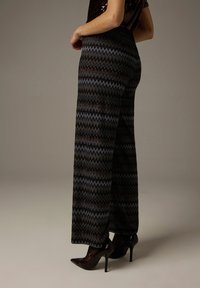 Gemusterte Hosen mit weitem Bein und Zickzackmuster in Schwarz, Blau und Bronzeakzenten. Aus einem strukturierten Material gefertigt, mit hoher Taille.