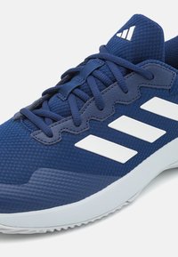 Sportowe sneakersy z siateczkowym cholewką w granatowym kolorze, teksturowanymi akcentami z gumy i białym logo w postaci trzech pasków. Posiadają dopasowane sznurówki i wyściełaną podeszwę.