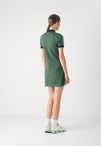 Rochie polo verde cu un model geometric, mâneci scurte și guler. Prezintă un bordaj contrastant și o croială slim, asortată cu adidași albi.