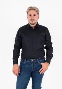 Camicia nera a maniche lunghe con bottoni, dal design aderente, texture liscia e colletto piatto, abbinata a jeans in denim blu.