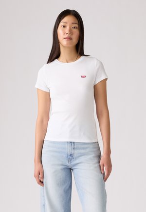 T-shirt blanc à manches courtes en coton doux, avec un petit logo rouge Levi's sur la poitrine ; associé à un jean bleu clair et ample.