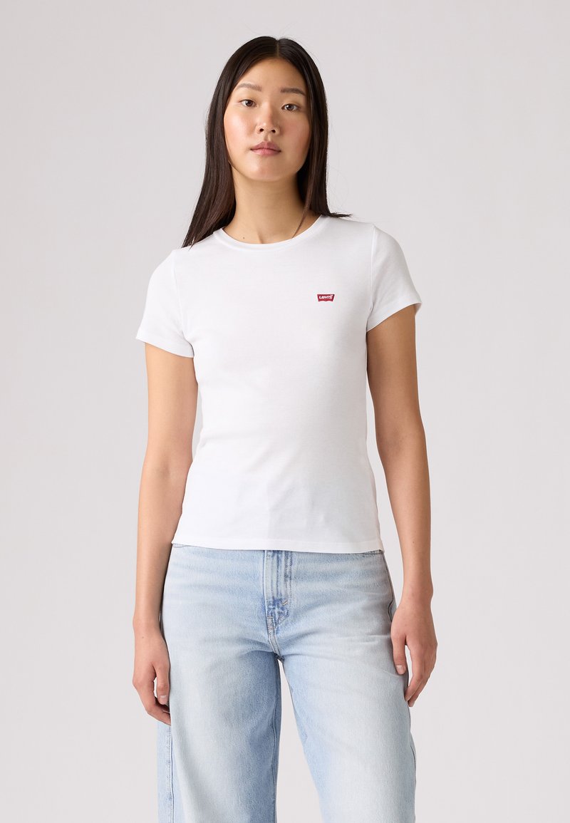 Hvid kortærmet t-shirt lavet af blødt bomuld, med et lille rødt Levi's-logo på brystet; parret med lyseblå, løstsiddende jeans.