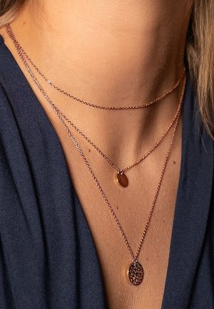 Tres collares de rosa oro en capas presentan delicadas cadenas con pequeños colgantes ovalados; uno de los colgantes tiene un patrón texturizado.