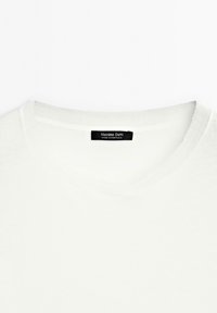 Hvid crewneck-T-shirt med en sort etiket, hvor der står "Massimo Dutti Made in Portugal", syet indvendigt.
