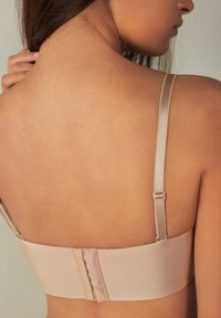 Nude beha met een gladde, satijnen textuur, verstelbare bandjes en een haak-en-oogsluiting aan de achterkant. Neutrale tint die de huid aanvult.