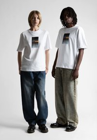 Biele bavlnené tričká s centrálnym grafickým potlačou, vo voľnom strihu, skombinované so voľnými džínami v rôznych odtieňoch a čiernymi topánkami.