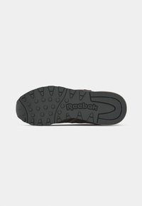 Sola de um sneaker Reebok castanho e preto com padrão de ranhura texturizado e logótipo Reebok centrado na sola de borracha preta.