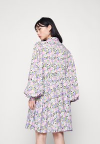 Vestido floral com padrões roxos, rosas e verdes. Apresenta mangas bufantes, gola e uma cintura franzida. O tecido parece leve.