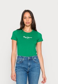 T-shirt verde de manga curta com decote redondo, apresentando o logótipo branco "Pepe Jeans London" no peito, combinado com jeans de cintura alta azuis.