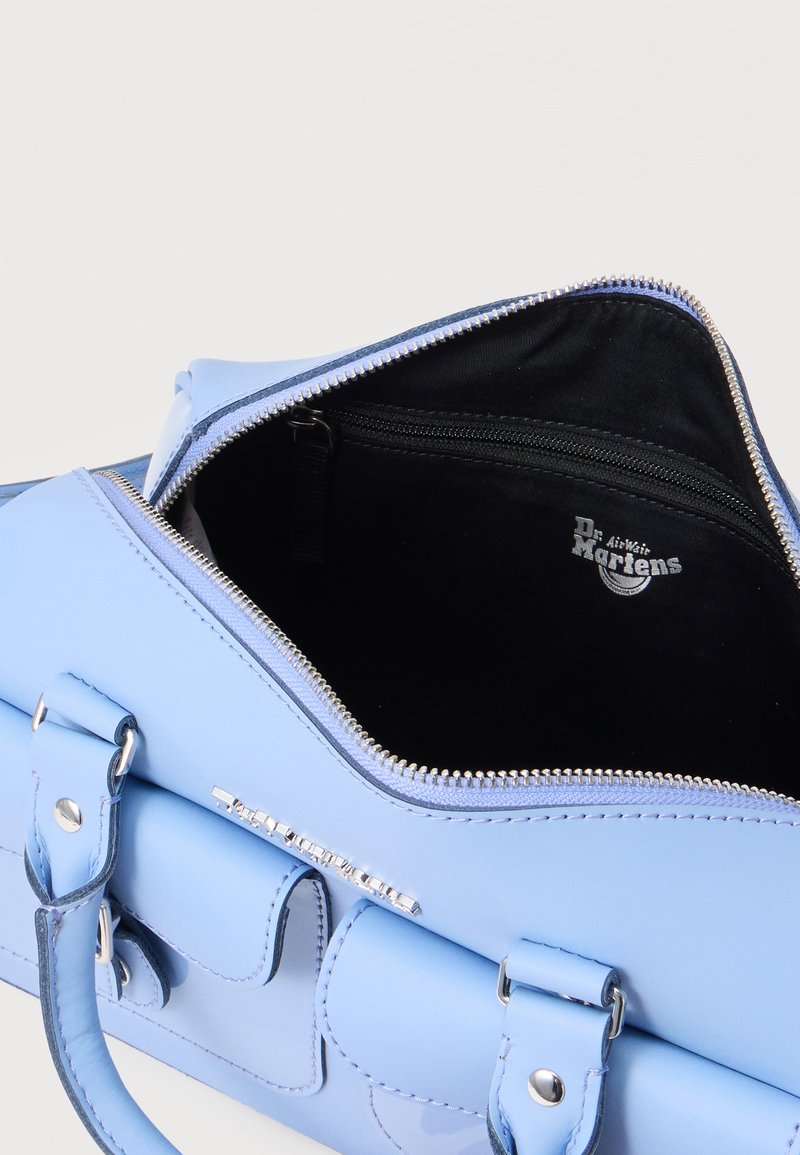 Hellblauer Lederhandtasche mit silbernem Reißverschluss, der teilweise geöffnet ist, und einem schwarzen Stoffinnenraum mit Dr. Martens-Logo sowie vorderen Schnallendetails.