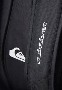 Black backpack featuring Quiksilver logo, durable textured material, and smooth accents, with a contrasting white graphic design.