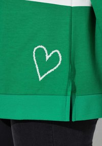 Groen katoenen top met een wit geborduurd hartdetail aan de zoom en geribbelde accenten, met zijsplitten voor extra comfort.