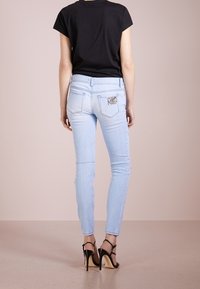 Jeans ajustados de color azul claro con decoloración, adornos en los bolsillos traseros, combinados con una blusa negra de manga corta y tacones altos negros con tiras.