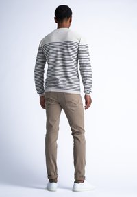 Suéter de rayas en crema y azul marino, combinado con pantalones beige. El conjunto presenta un diseño casual con puños acanalados y detalles en la parte trasera.