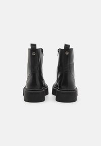 Botas de cuero negro hasta el tobillo con punteras redondeadas, suela texturizada y cierres de cremallera, con una pestaña en la parte trasera y detalle del logo en el tacón.