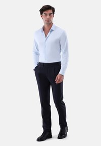 Hellblaues Hemd mit langen Ärmeln, kombiniert mit dunklen marineblauen Hose. Schwarze Anzugschuhe vervollständigen das Outfit. Glatte Textur, ordentlicher Schnitt.