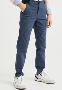 Námořnické modré, slim-fit kalhoty vyrobené z texturované tkaniny s předním zapínáním na knoflík a bočními kapsami. Kombinováno s bílými teniskami.