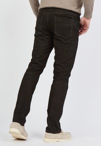 Czarne zamszowe spodnie o dopasowanym kroju, z tylnymi kieszeniami i teksturowaną powierzchnią, zestawione z jasnymi, casualowymi butami.